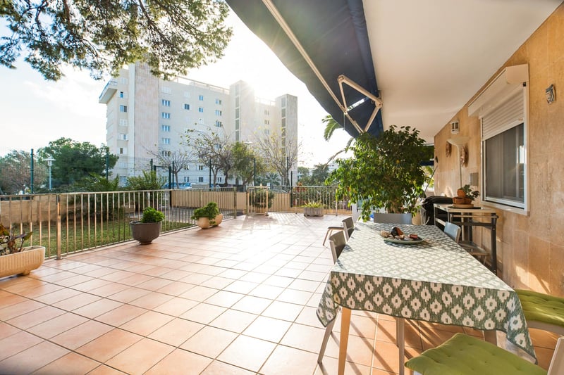 Vaste terrasse extérieure avec carrelage en terre cuite, table à manger sous un store et murs en pierre naturelle.
