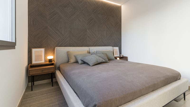 Chambre moderne avec mur d'accent géométrique en bois, lit rembourré gris et tables de nuit en noyer.