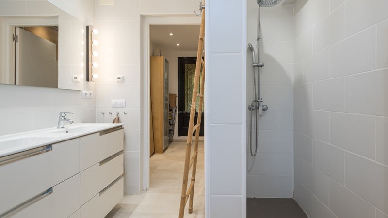 Salle de bain lumineuse avec carrelage blanc, grande douche à l'italienne et double vasque blanche.
