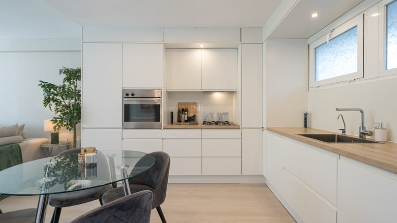 Cuisine minimaliste blanche avec four Miele, plan de travail effet bois et table à manger en verre.
