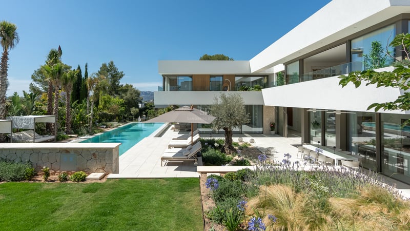 Villa moderne blanche avec une longue piscine turquoise, des bains de soleil et un jardin paysager méditerranéen.