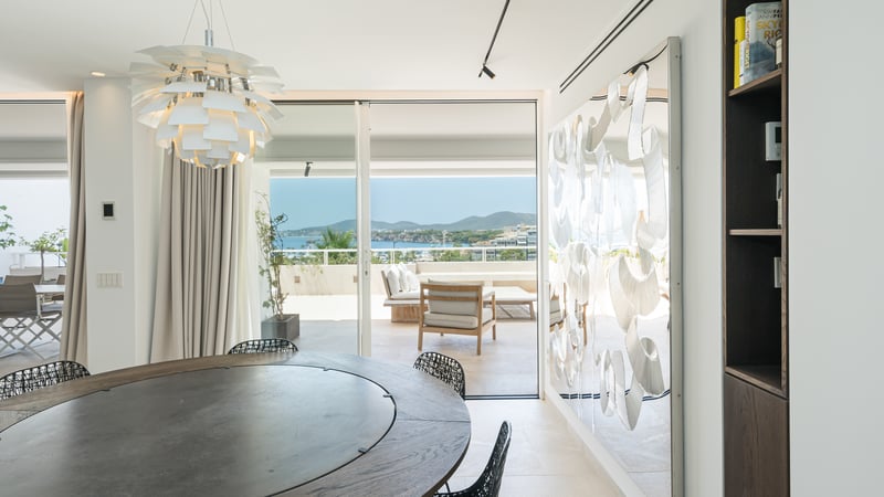 Salle à manger de luxe avec table ronde, suspension design et baies vitrées donnant sur une baie méditerranéenne.