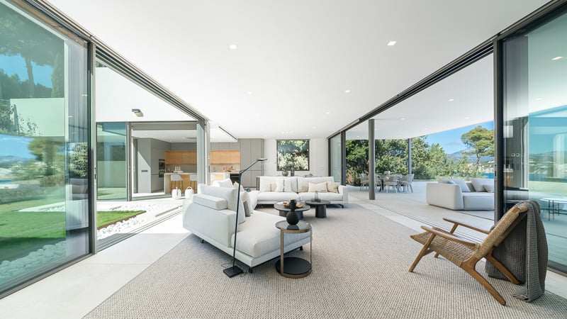 Salon moderne et lumineux avec de grandes baies vitrées ouvrant sur le jardin, comprenant des canapés blancs.