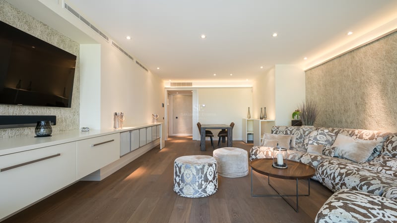 Salon moderne avec canapé à motifs, parquet en bois sombre et meuble TV intégré sous un éclairage chaleureux.