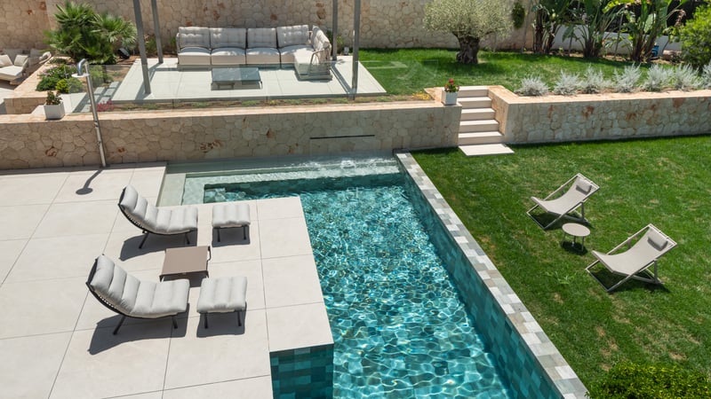 Vue d'en haut d'une piscine turquoise, chaises longues de designer sur patio et pelouse impeccable.