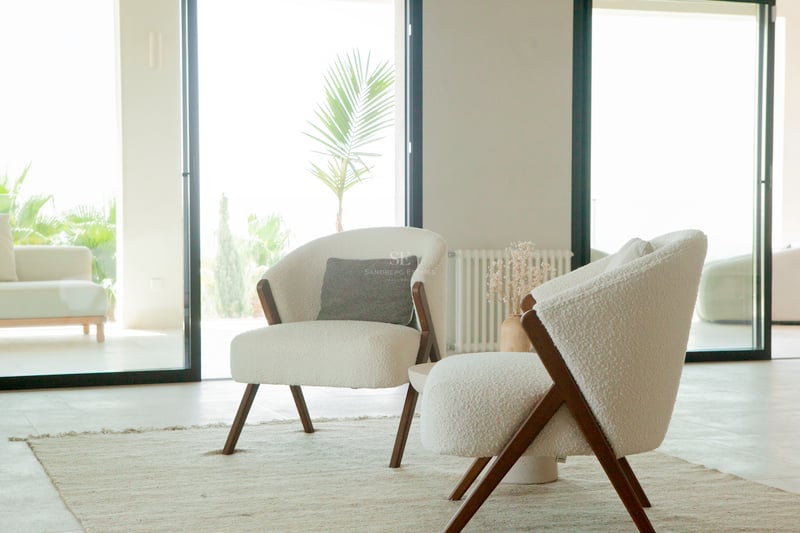 Deux fauteuils en bouclé blanc avec cadres en bois sur un tapis de jute dans un salon lumineux ouvrant sur une terrasse.