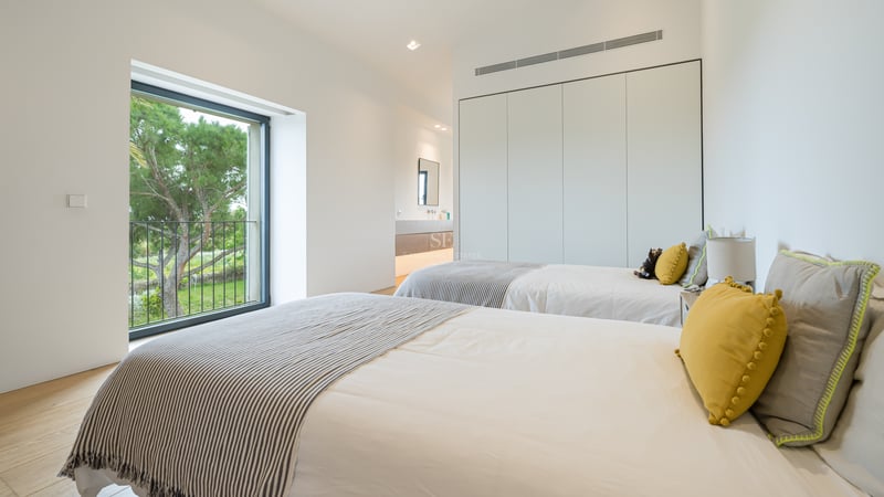 Chambre minimaliste avec lits jumeaux, parquet en chêne clair et grande fenêtre donnant sur des pins méditerranéens.