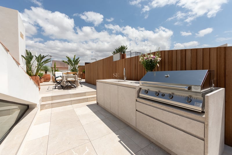 Terraza contemporánea con cocina exterior de piedra, barbacoa integrada, valla de madera y zona de comedor al aire libre.
