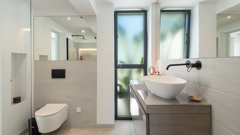 Salle de bain contemporaine avec vasque à poser blanche, robinetterie noir mat, WC suspendu et grands miroirs.