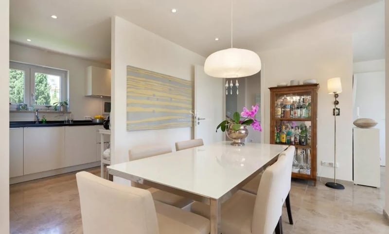Salle à manger contemporaine avec sol en marbre, table blanche et chaises crème à côté d'une cuisine moderne.