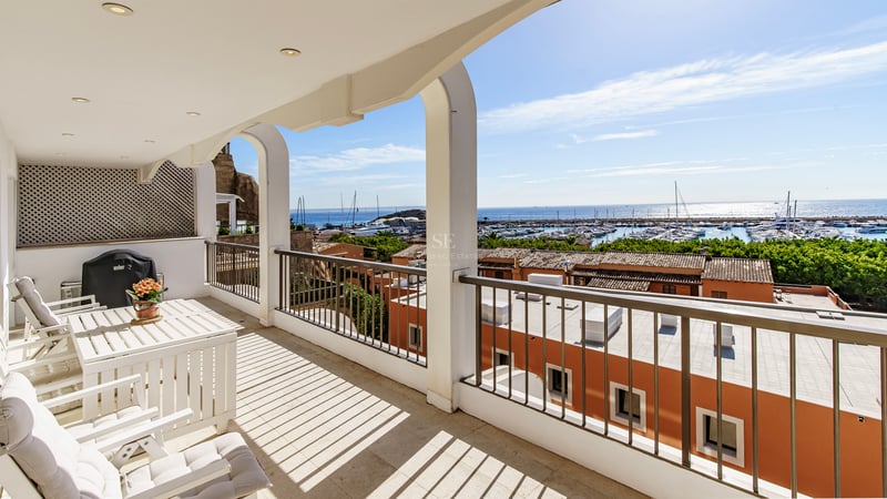Balcon blanc avec arches et mobilier d'extérieur offrant une vue sur un port de plaisance et la mer bleue.