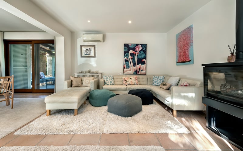 Salon moderne avec canapé en cuir blanc, poufs colorés, tapis à poils longs et cheminée à bois.