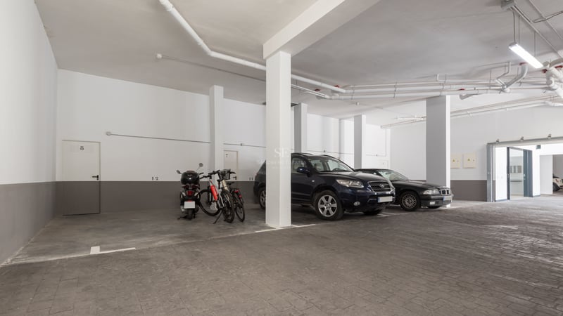 Parking souterrain avec piliers blancs, sol en pierre grise et voitures garées sous un éclairage artificiel.