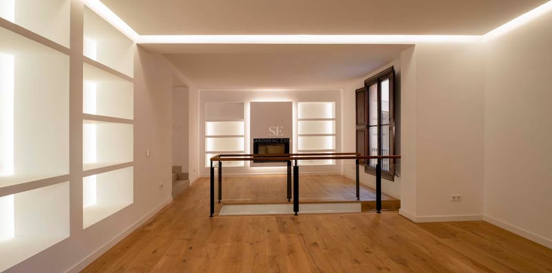 Intérieur minimaliste avec parquet en chêne, murs blancs avec niches éclairées et garde-corps en verre.