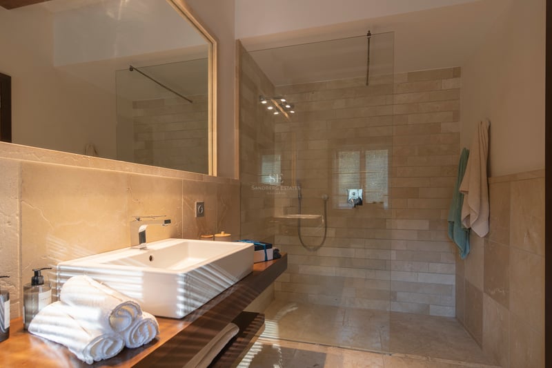 Salle de bain contemporaine avec douche en verre, pierre naturelle et vasque sur plan de travail en bois.