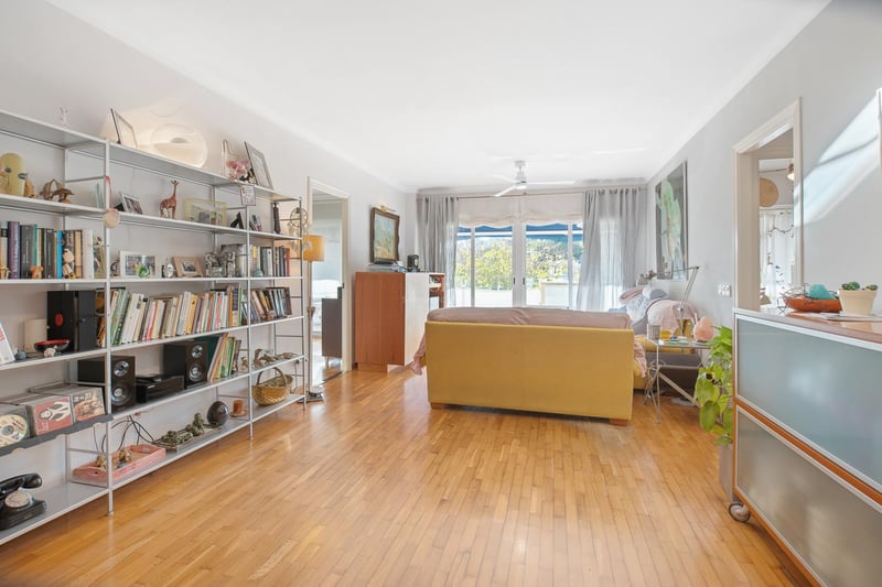 Salon spacieux avec parquet en chêne miel, grande étagère métallique et baies vitrées ouvrant sur un balcon.