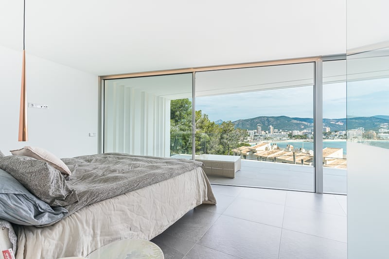 Chambre lumineuse avec grand lit et baies vitrées ouvrant sur une terrasse surplombant la côte et les montagnes.