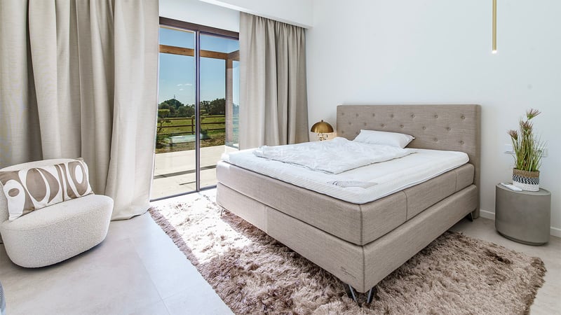 Chambre de luxe avec lit capitonné, tapis moelleux et grandes baies vitrées ouvrant sur un jardin.