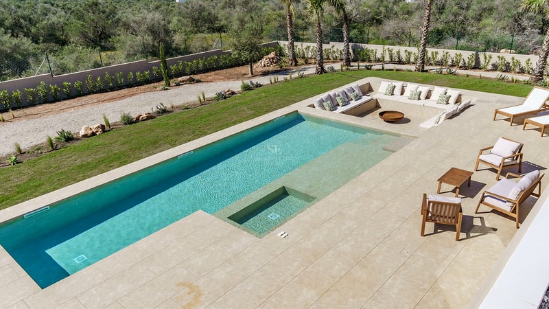 Piscine rectangulaire turquoise avec terrasse en pierre naturelle et coin salon encastré avec coussins et brasero.