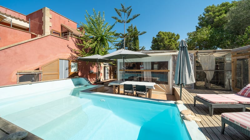 Piscine turquoise à côté d'une terrasse en bois avec bains de soleil et façade ocre sous un ciel bleu.