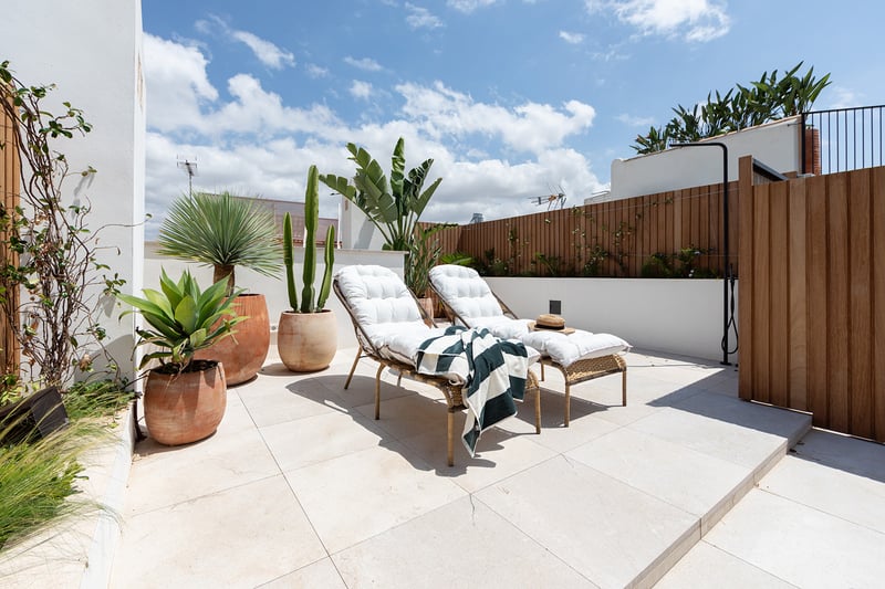 Terraza moderna en la azotea con dos tumbonas blancas, grandes macetas de terracota con cactus y valla de madera.