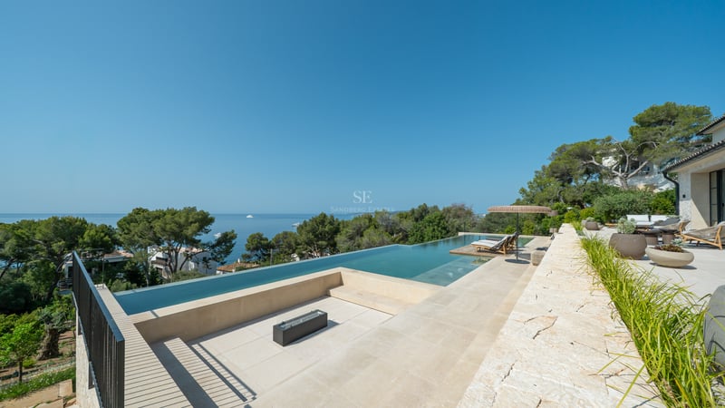 Vue en plongée d'une piscine à débordement de luxe et d'un coin salon avec brasero surplombant la Méditerranée.