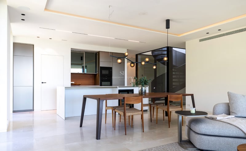 Salle à manger à aire ouverte avec table en noyer, îlot de cuisine blanc et éclairage contemporain dans une villa.