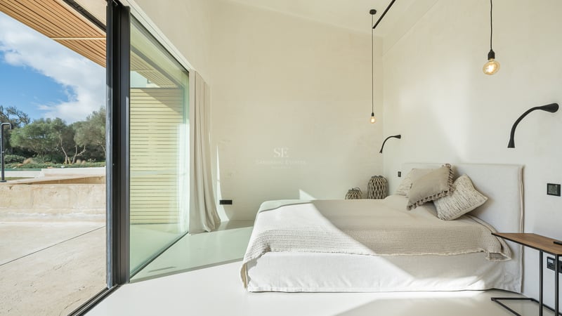 Chambre lumineuse au design minimaliste avec lit blanc, grandes baies vitrées et balcon privé.