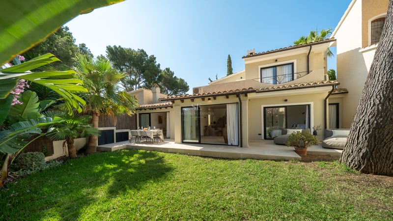 Vue extérieure d'une villa crème avec toit en terre cuite, pelouse et grandes baies vitrées coulissantes.