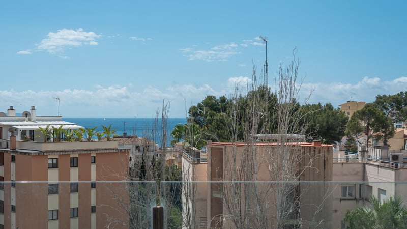Vue de la mer Méditerranée et des bâtiments côtiers à travers un garde-corps en verre sous un ciel bleu.