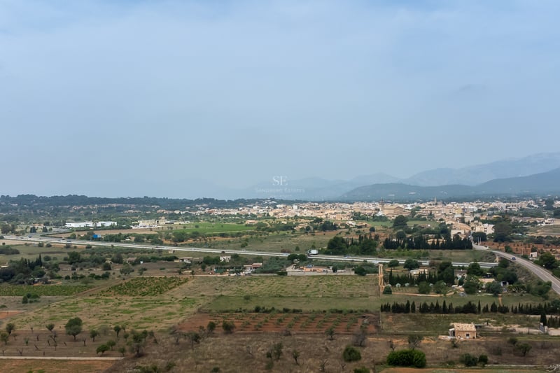 Vaste paysage d'un village majorquin entouré de champs agricoles et de montagnes sous un ciel voilé.