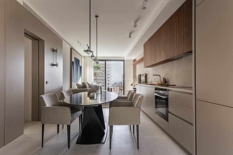 Salle à manger contemporaine avec table ovale noire, chaises grises et cuisine minimaliste avec vue sur balcon.