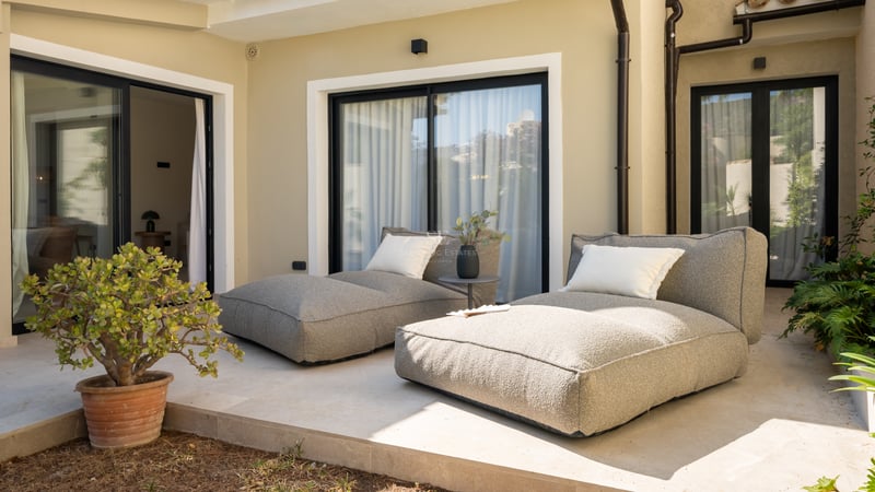Deux chaises longues en tissu gris sur une terrasse en pierre naturelle devant des baies vitrées et une plante grasse.