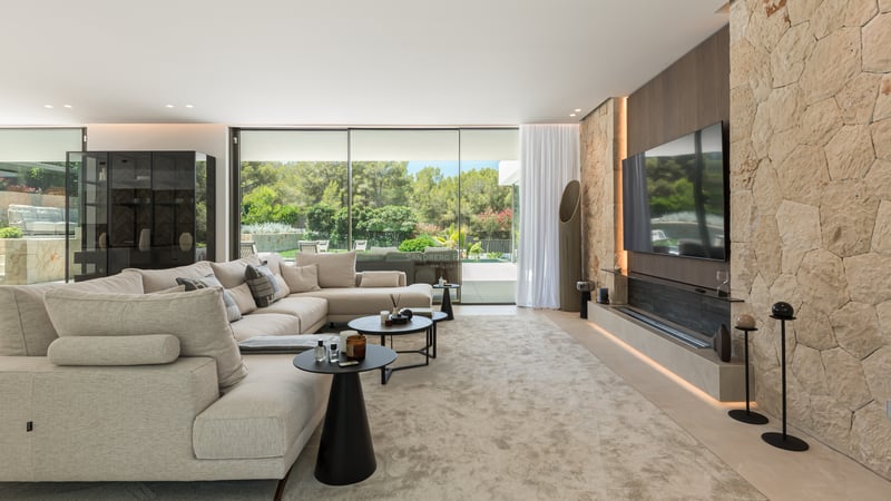 Vaste salon moderne avec mur en pierre naturelle, grand canapé beige et baies vitrées donnant sur le jardin.