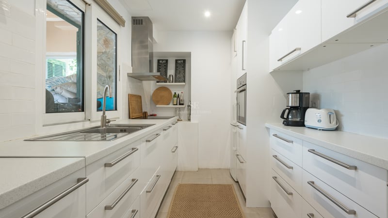 Cuisine lumineuse avec placards blancs brillants, plans de travail en quartz et appareils en inox.