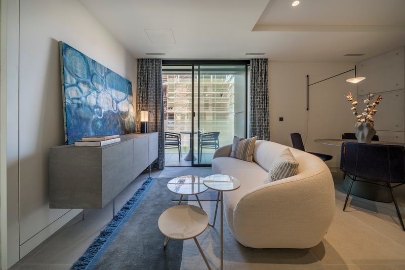 Salon contemporain avec canapé incurvé blanc, buffet en béton et grandes baies vitrées ouvrant sur un balcon.