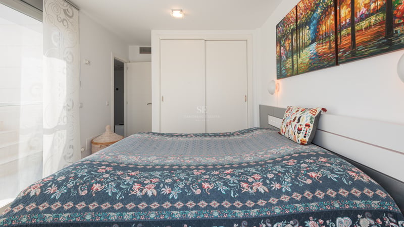 Chambre lumineuse avec un grand lit, un triptyque coloré, un placard coulissant blanc et un accès extérieur.