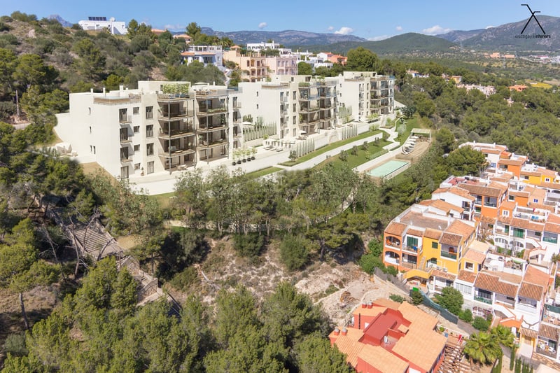 Vue aérienne d'un complexe d'appartements moderne sur une colline avec terrasses privées et piscine commune.