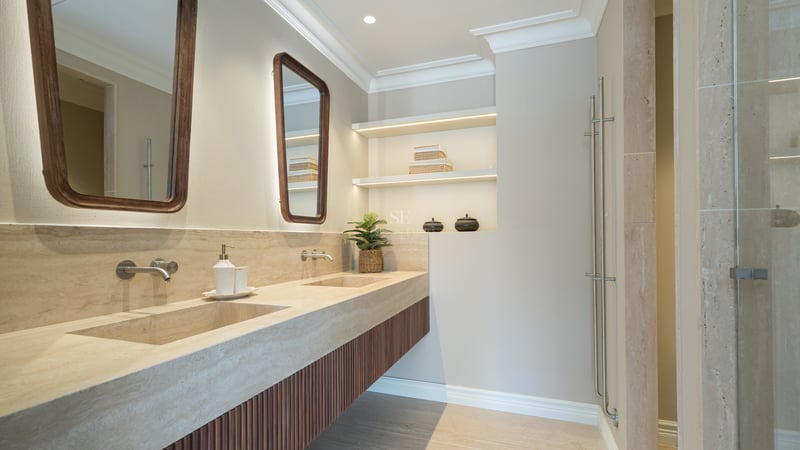 Modern bathroom featuring a dual travertine stone vanity, wood-slat cabinets, and LED-lit recessed shelving.