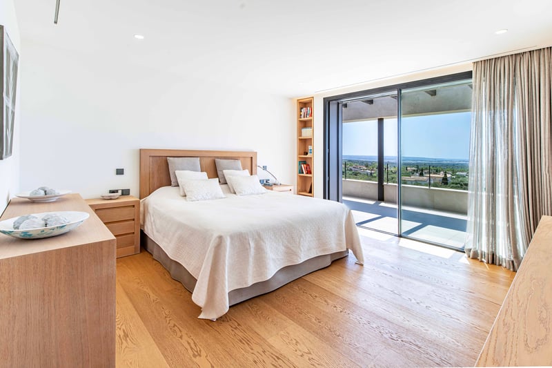 Chambre lumineuse avec parquet en chêne clair et baies vitrées toute hauteur ouvrant sur une terrasse avec vue mer.