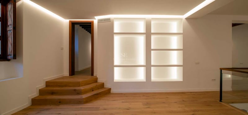 Pièce moderne avec parquet en bois, marches en chêne et étagères encastrées éclairées par des lumières LED chaleureuses.