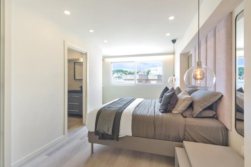 Chambre moderne avec tête de lit en velours rose, suspensions en verre et accès à la salle de bain attenante.