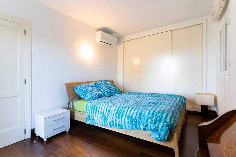 Chambre avec lit en bois, literie bleue, murs blancs, parquet foncé et placard intégré.