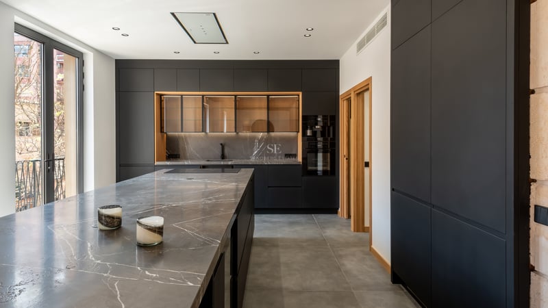 Cuisine moderne avec placards noir mat, plan de travail en marbre gris veiné et grandes fenêtres.