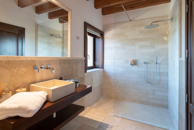 Salle de bain contemporaine avec murs en pierre naturelle, douche à l'italienne et poutres en bois apparentes.