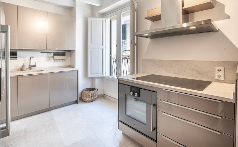 Cuisine moderne lumineuse avec placards beige brillant, plan de travail en pierre et porte-fenêtre.