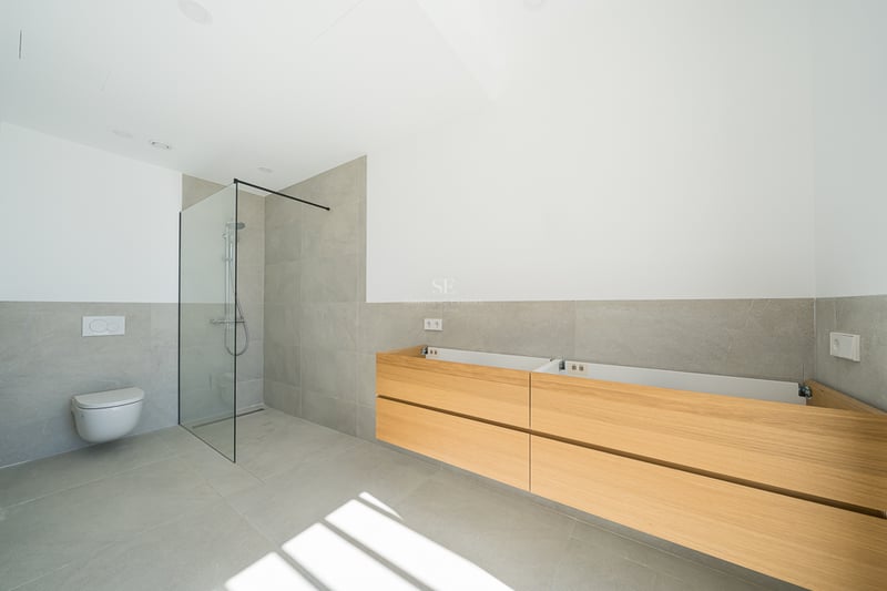 Salle de bain moderne avec carrelage gris, douche à l'italienne en verre, WC suspendu et meuble en bois.