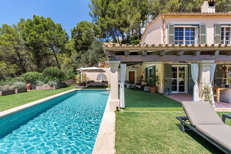 Piscine rectangulaire turquoise à côté d'une villa méditerranéenne avec terrasse couverte et volets verts.