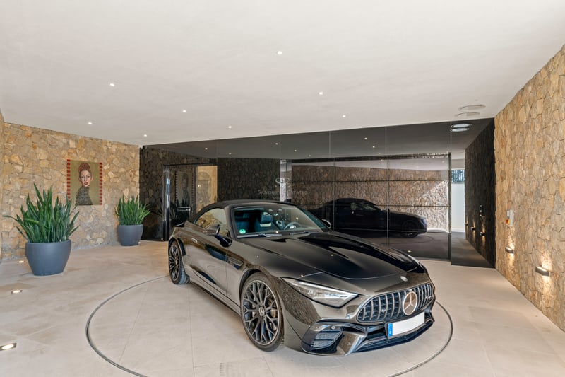 Une Mercedes de sport noire sur une plateforme rotative circulaire dans un garage moderne avec des murs en pierre.