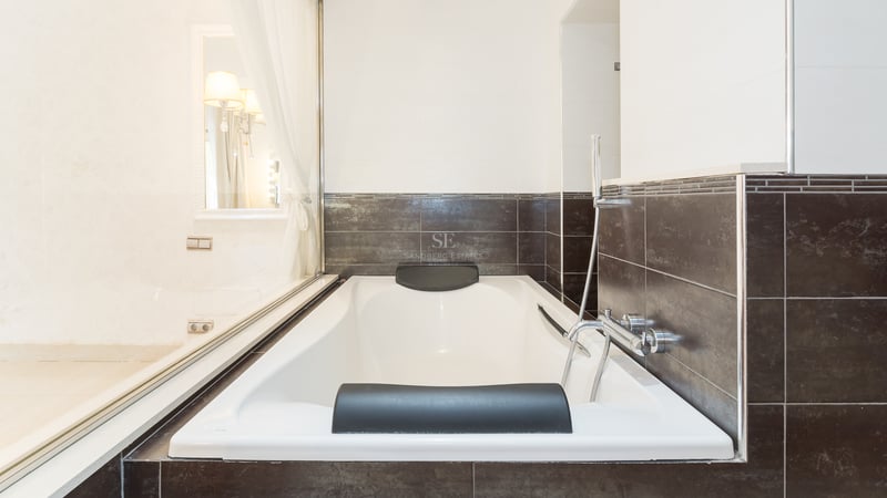 Baignoire blanche avec appuie-tête noirs et carrelage marron foncé dans une salle de bain moderne.